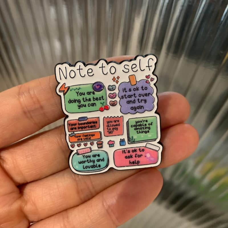 Colorful 'Note to self' motivational enamel pin held in a hand