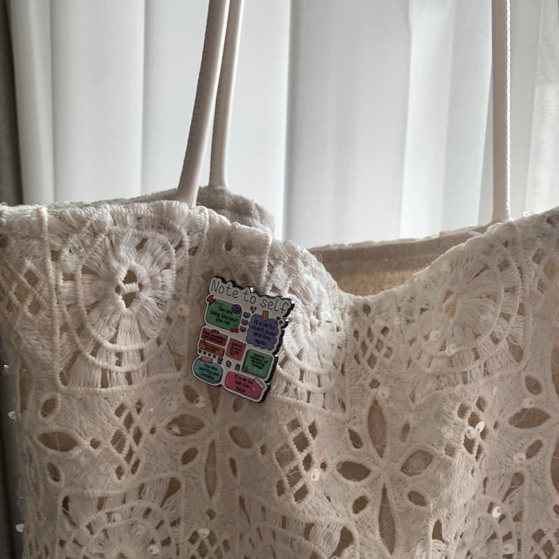 White lace bag with a colorful pin against a white curtain background